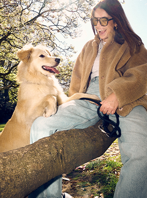 Frauchen sitzt mit ihrem Hund auf einem Baumstamm und lacht Frauchen sitzt mit ihrem Hund auf einem Baumstamm und lacht